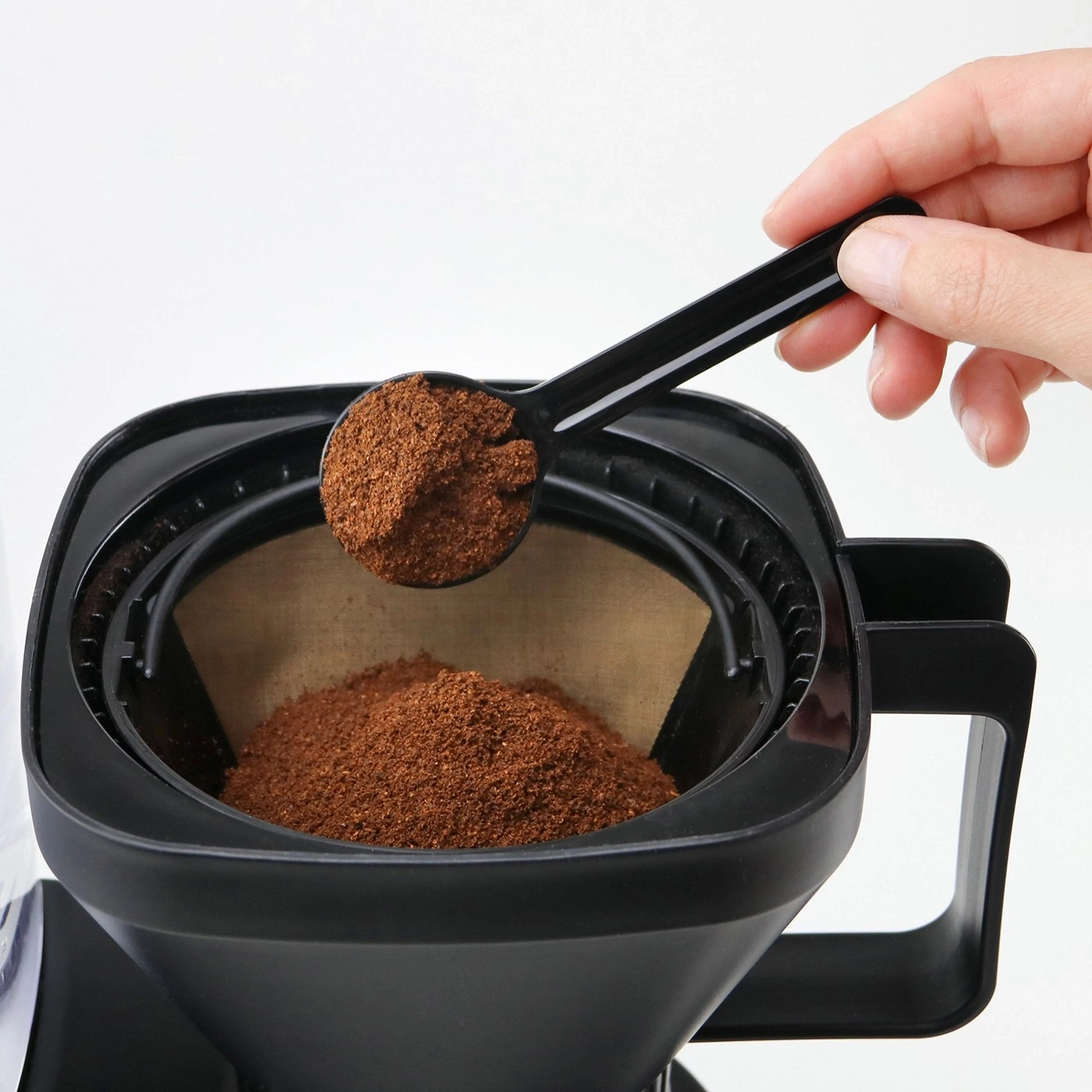 Coffee grounds being poured into a coffee filter with a black scoop.