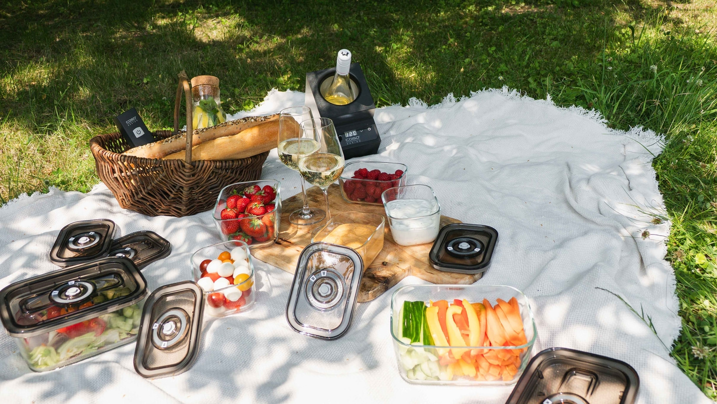 Picknick im Freien mit Essen, Getränken und Decke auf dem Rasen.
