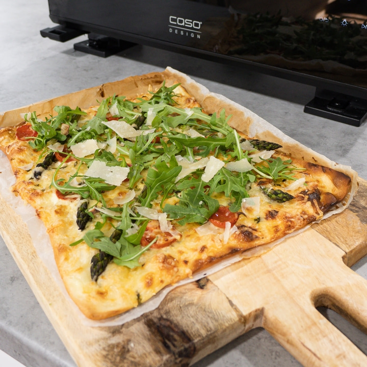 Pizza mit Rucola, Spargel und Parmesan auf einem Holzbrett