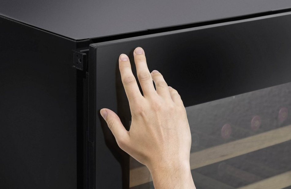 Eine Hand berührt die schwarze Tür eines Weinkühlschranks.