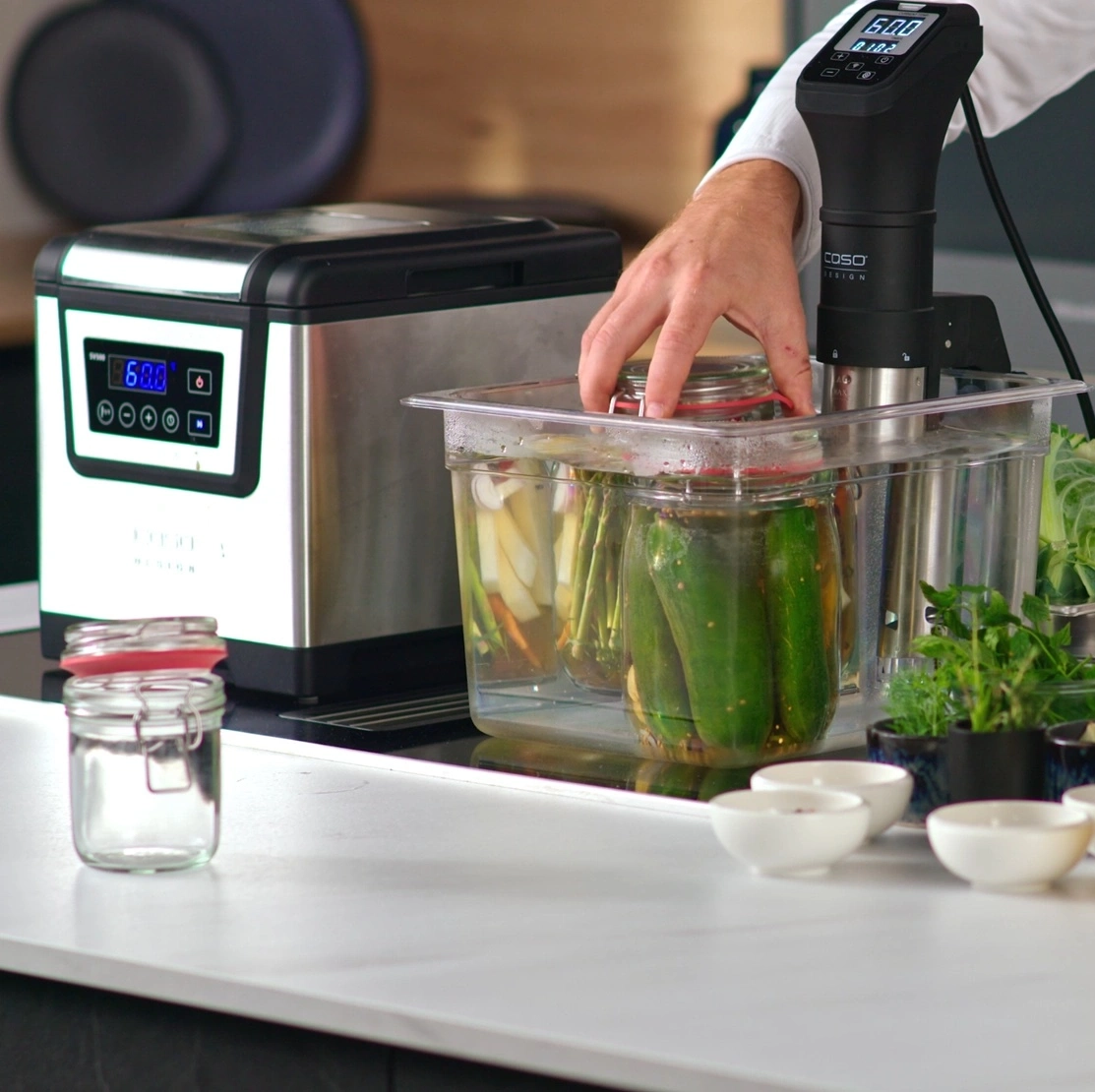 Ein Mann kocht Gemüse in einem Sous-Vide-Gerät, das in einem Wassertank steht.
