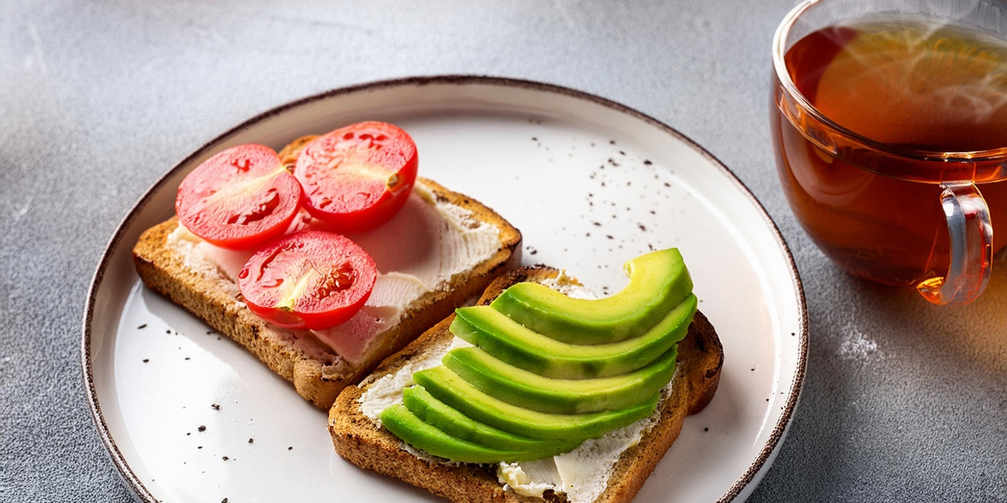 Geröstetes Brot mit Tomaten, Avocado und Tee auf einem Teller