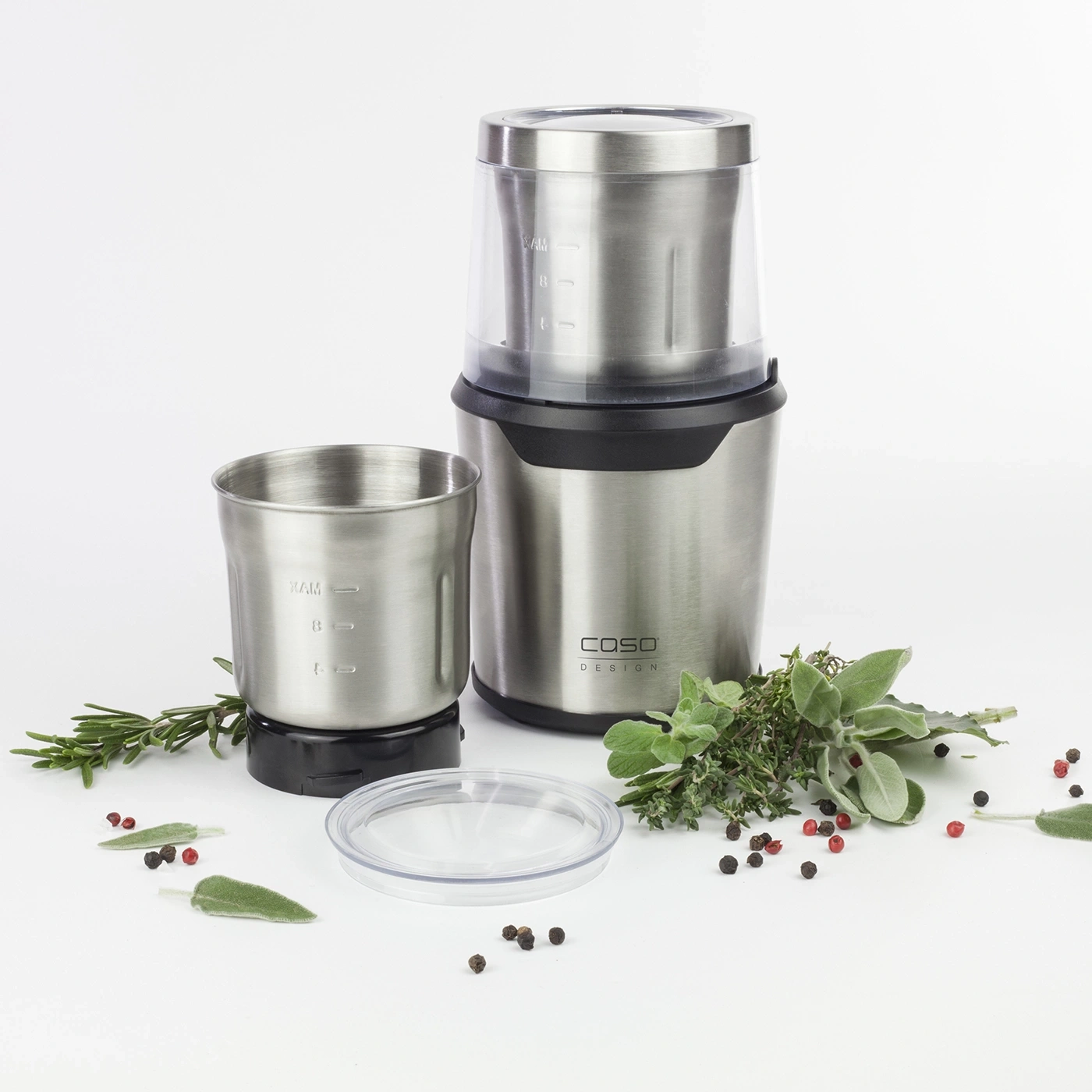 Stainless steel coffee grinder with herbs and spices on a white background.