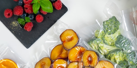 Beeren, Pflaumen, Brokkoli und Orange in Vakuumbeuteln auf weißem Hintergrund.