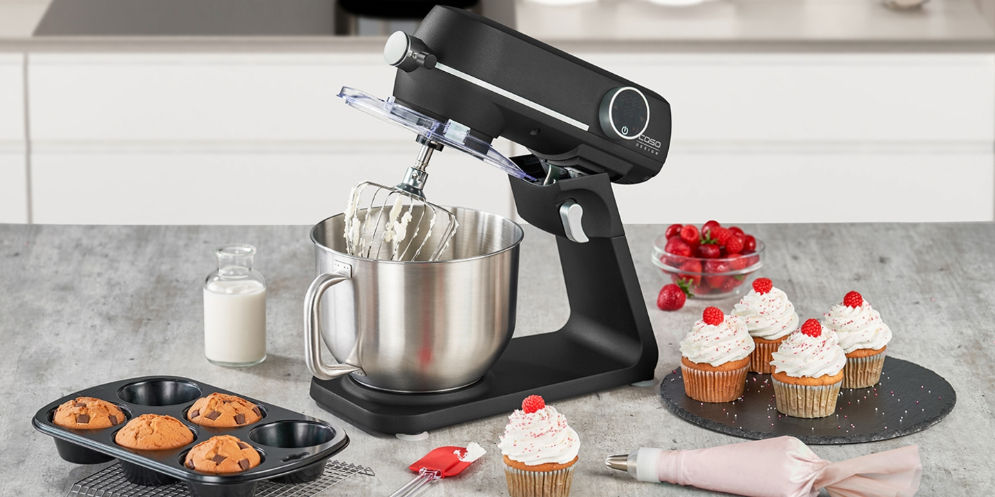 Küchenmaschine mit Cupcakes, Himbeeren und Milch in einer Glasflasche auf einem Tisch