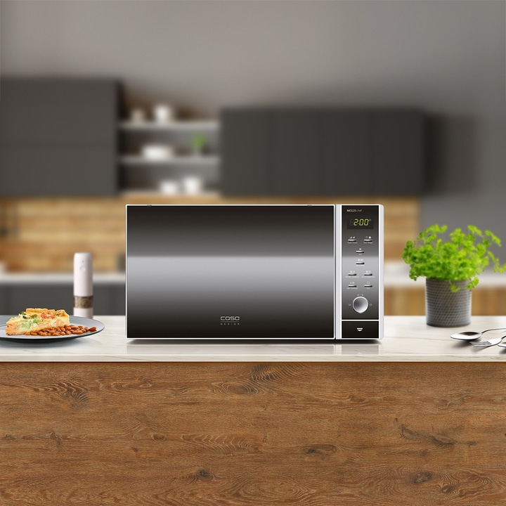 Microwave on a kitchen counter with food and plant in the background