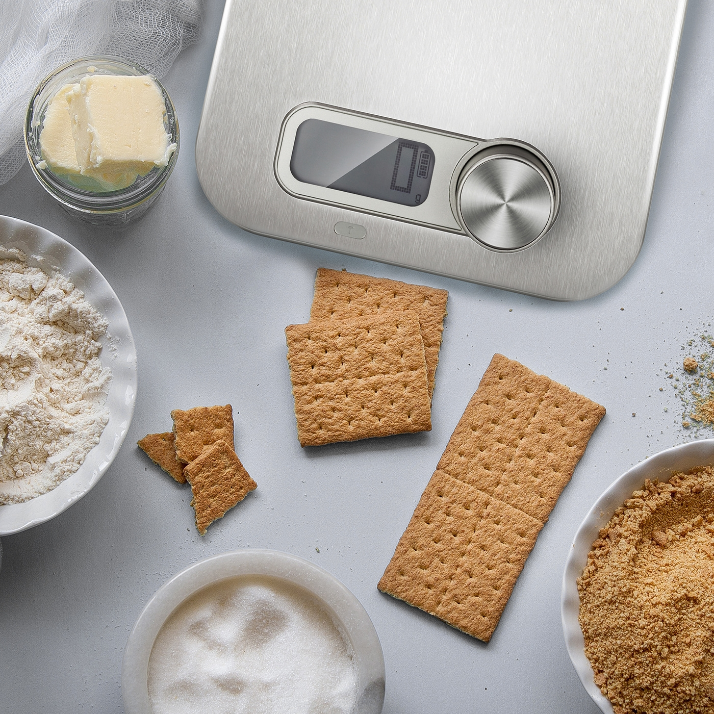 Ingredients for a cake: butter, flour, sugar, graham crackers, and a scale.