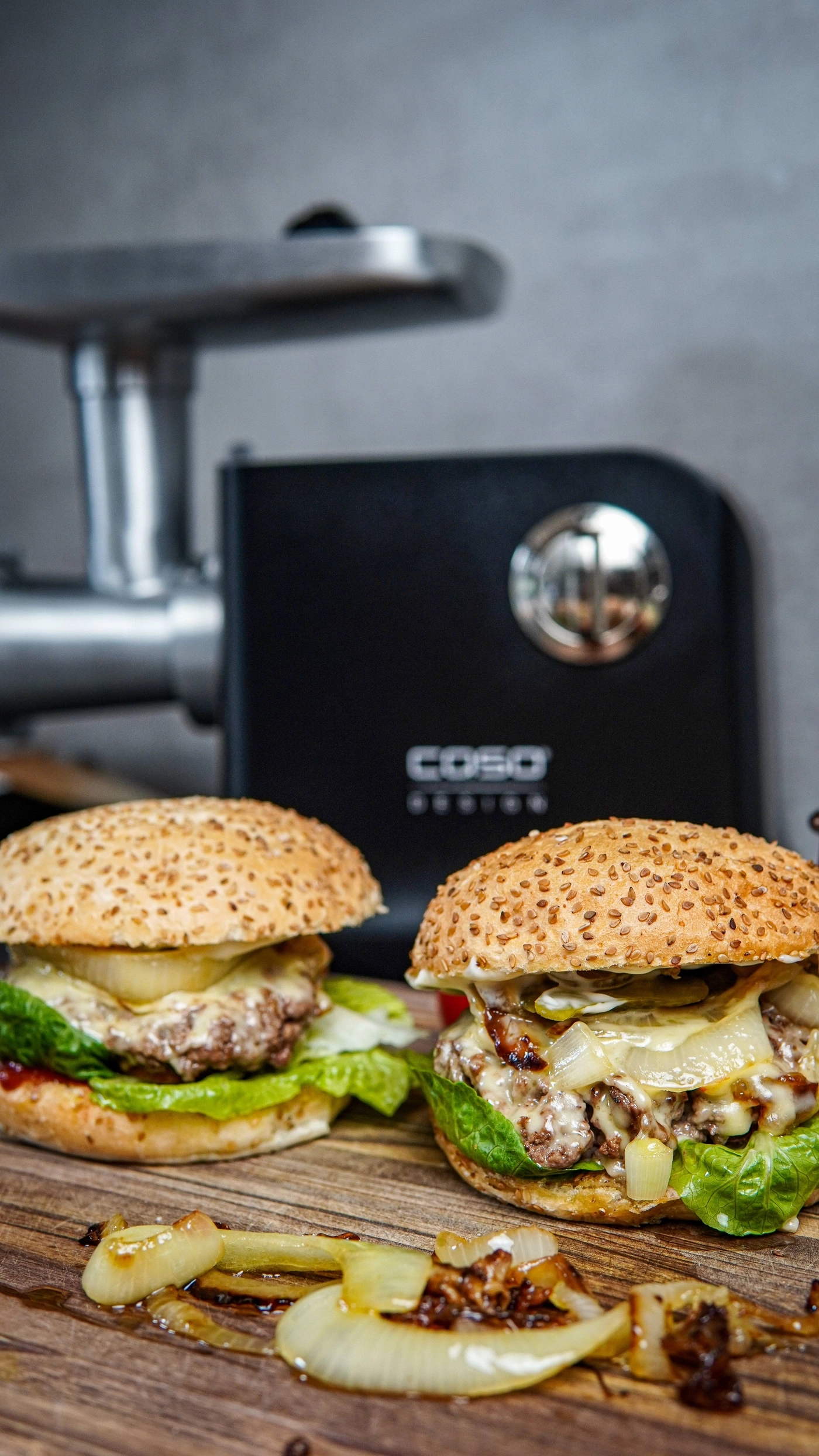 Zwei Burger mit Käse, Salat und Zwiebeln, daneben eine Küchenmaschine.