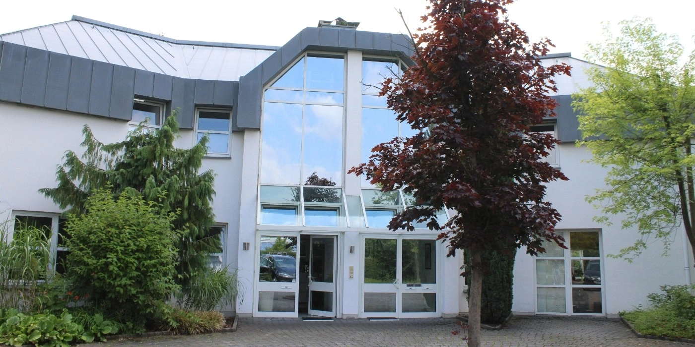 Building with glass facade and trees, entrance area with open door.