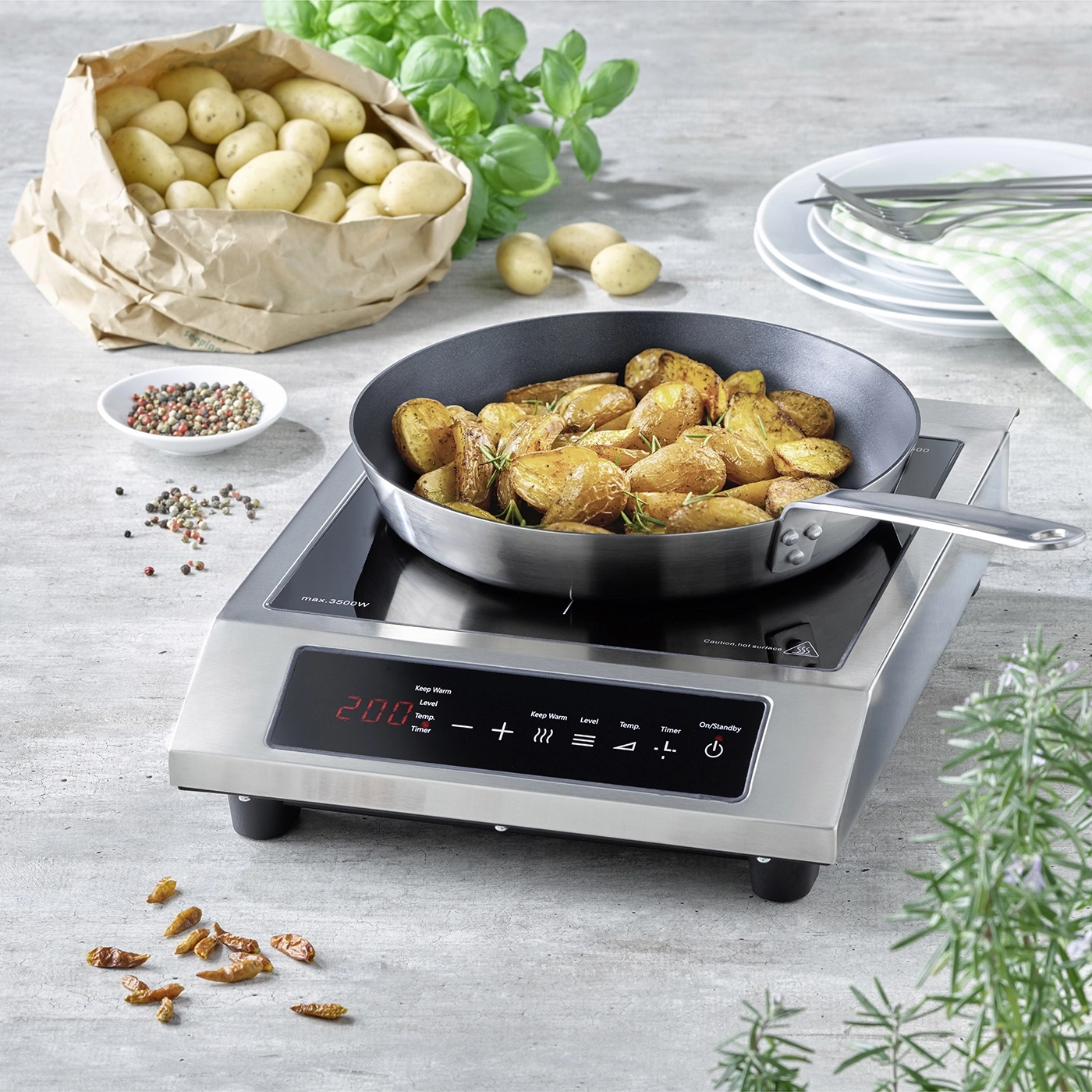 Roasted potatoes in a pan on an induction cooktop with ingredients and plates.