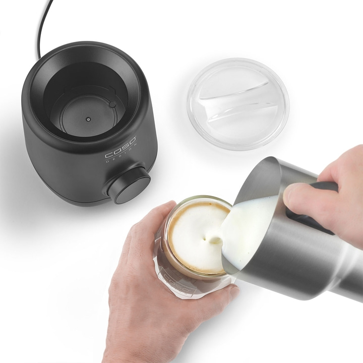 Milch wird in ein Glas mit Kaffee gegossen, daneben ein Milchaufschäumer.