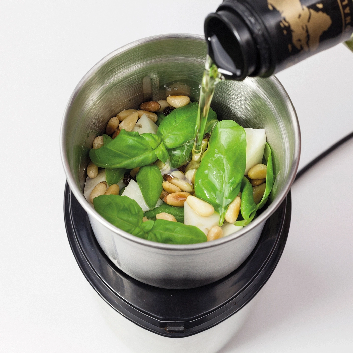 Pesto ingredients in a blender, oil being added, close-up, cooking process, kitchen