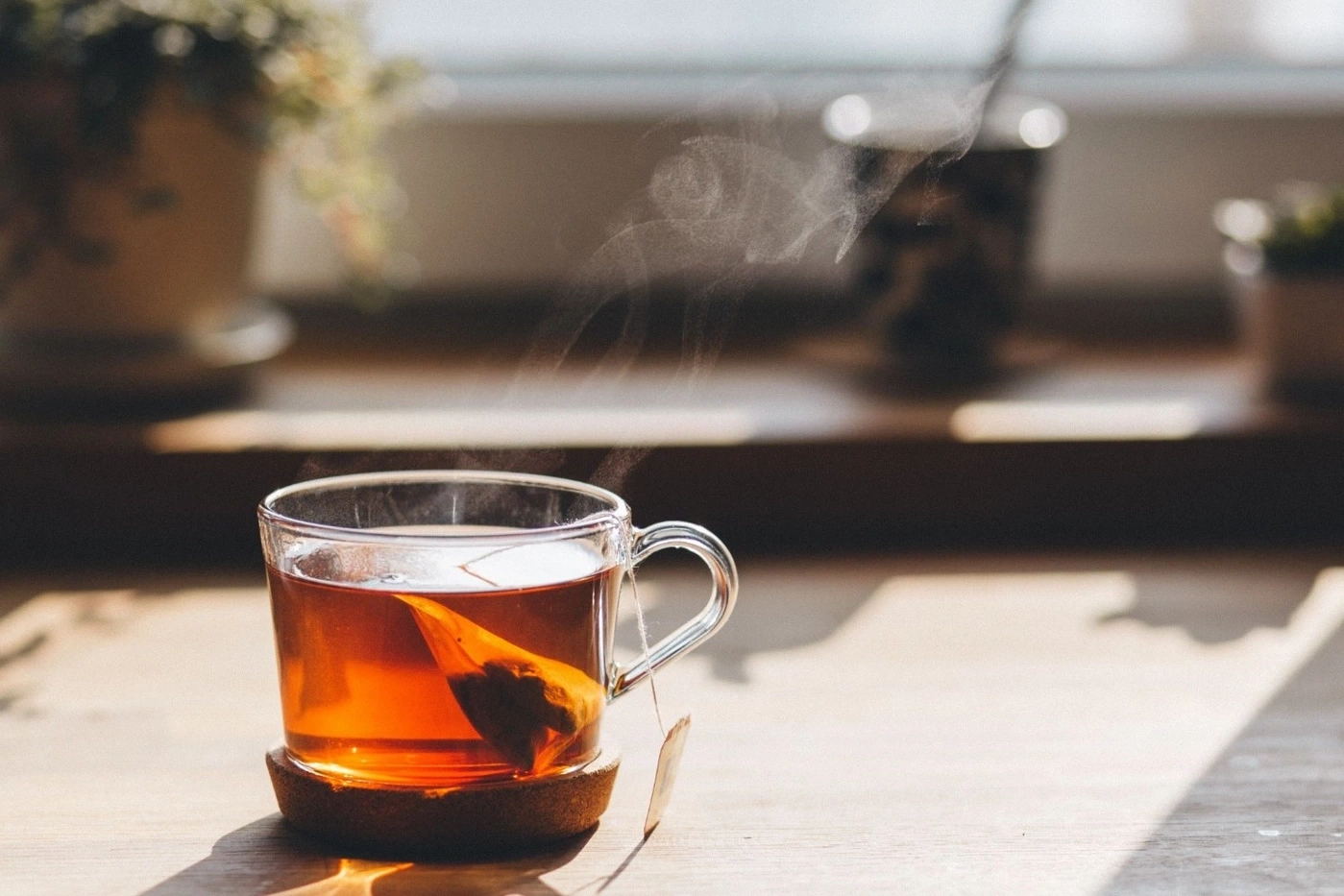 A glass of tea with a tea bag on a wooden board, steaming, sunny.