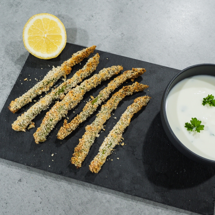 Fried asparagus with lemon and dip on a black serving board