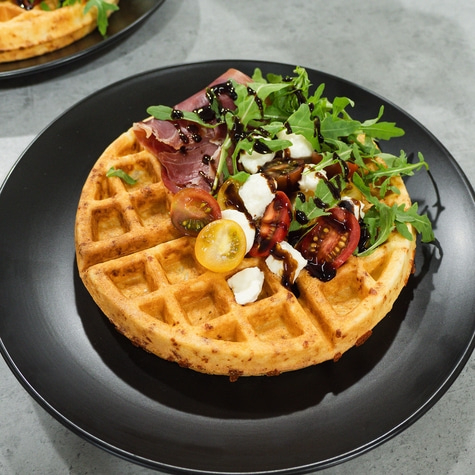 Waffle with tomatoes, cheese, arugula, and balsamic glaze on a black plate