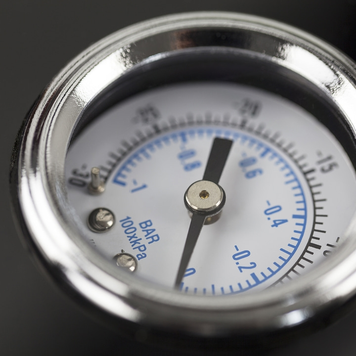 Nahaufnahme eines Manometers mit schwarzem Zeiger und blauen Markierungen auf weißem Zifferblatt