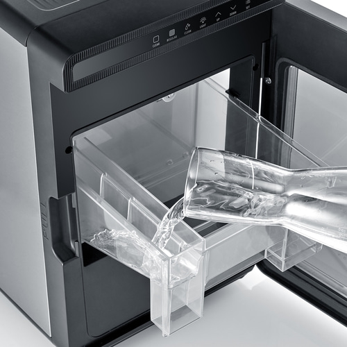Wasser wird in einen Eisbereiter gegossen, der sich in einem Schrank befindet.