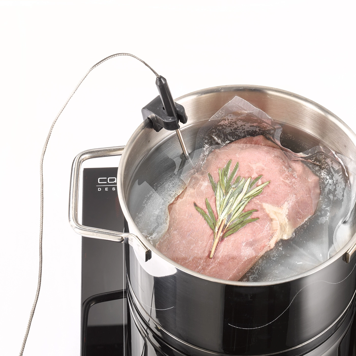 Meat being sous vide in a pot of water, with rosemary, and a thermometer.