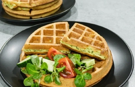 Waffeln mit Salat und Tomaten auf einem schwarzen Teller