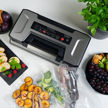 Vacuum sealer with fruits, vegetables, fish, herbs, and fruits on a white table.