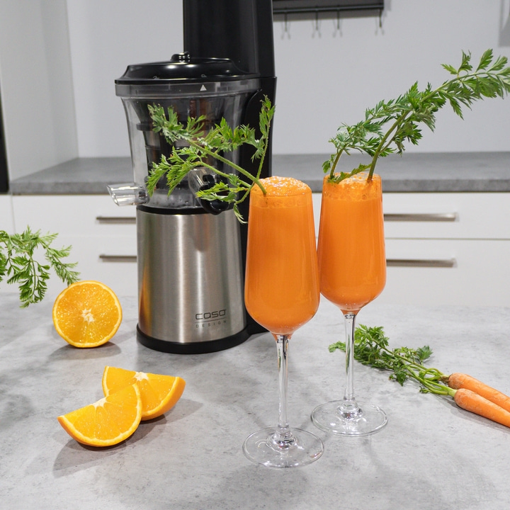 Zwei Gläser Karottensaft mit Karottenkraut, Orangen und Entsafter.