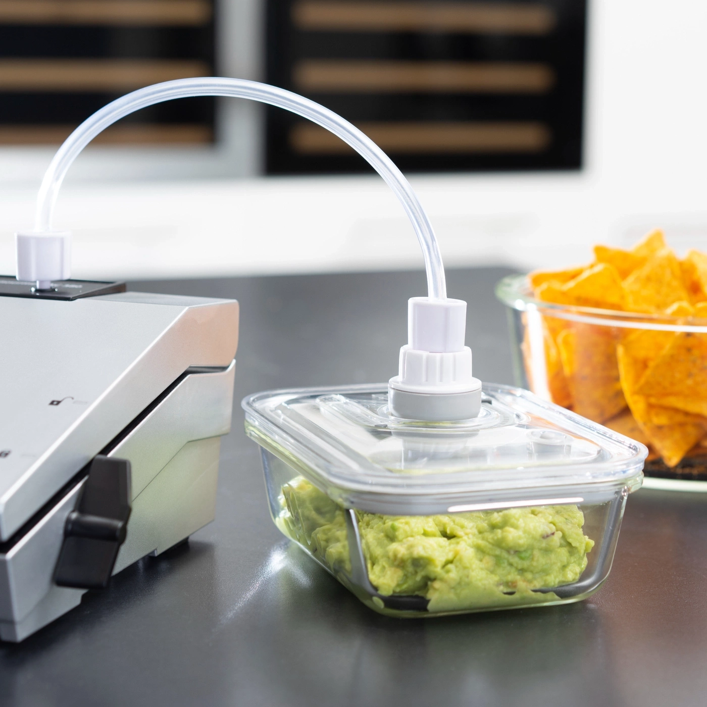 Vakuumiergerät mit Guacamole und Chips in Glasbehältern auf dunklem Tisch