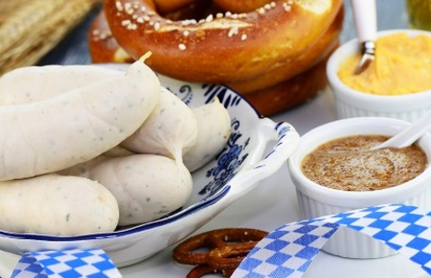 White sausages, pretzels, mustard, and blue and white ribbon on a table