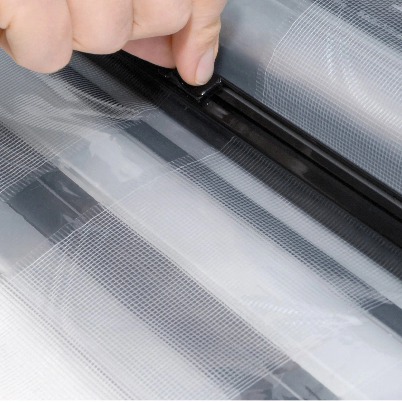 Close-up of a hand operating a black clasp on transparent plastic wrap, detail.