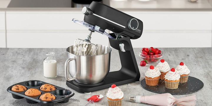 Stand mixer with cupcakes, raspberries, and milk in a glass bottle on a table