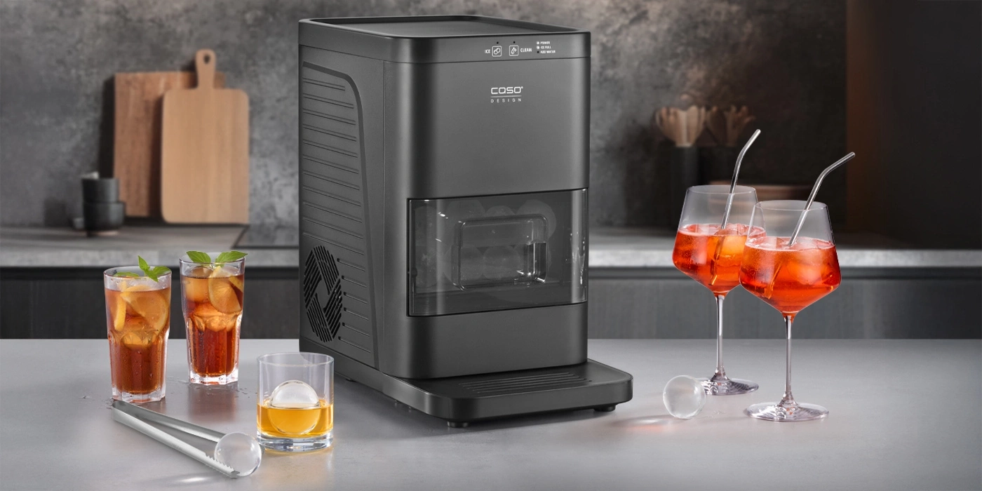 Ice maker with glasses of drinks and ice cubes on a countertop.
