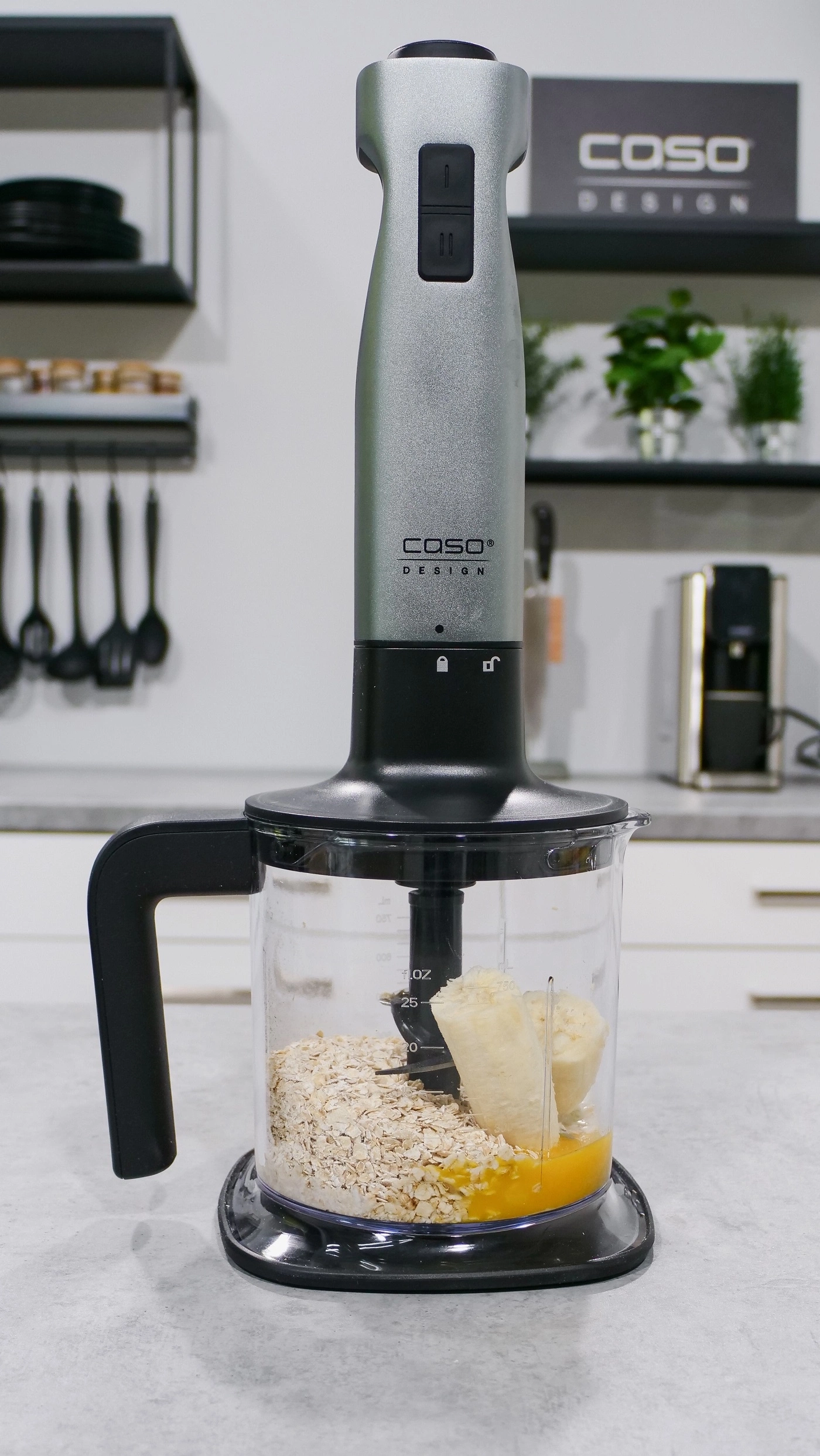 Mixer mit Zutaten: Haferflocken, Banane und Flüssigkeit in einem Becher.