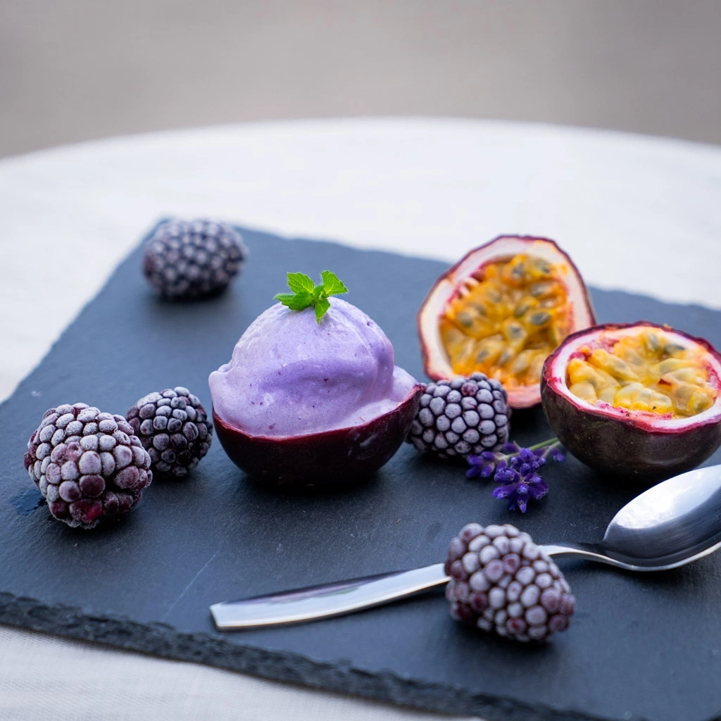 Purple ice cream in passion fruit with blackberries and mint on a black board