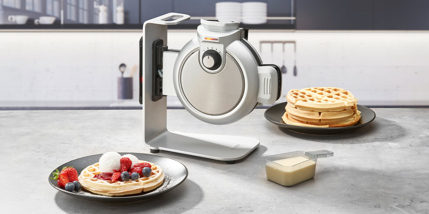 Waffeleisen mit Waffeln und Beeren auf einem Teller, Eis und Soße.