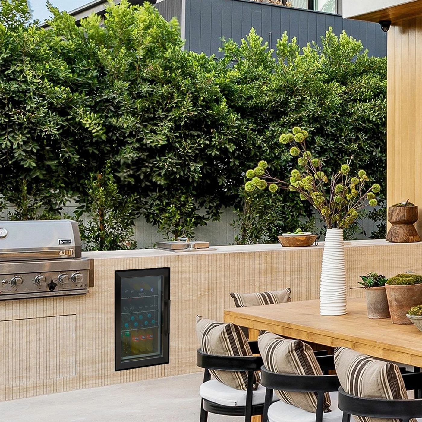 Outdoor kitchen with grill, fridge, table, chairs, plants, and decorative elements.