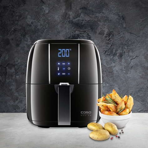 Schwarze Heißluftfritteuse mit Pommes Frites und Kartoffeln auf einem Tisch