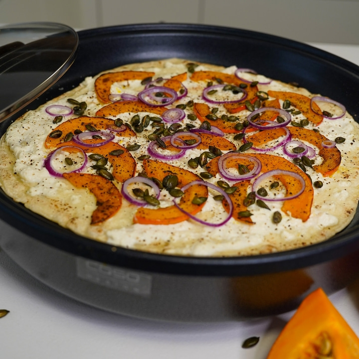 Pumpkin pizza with onions and seeds in a black pan, close-up shot