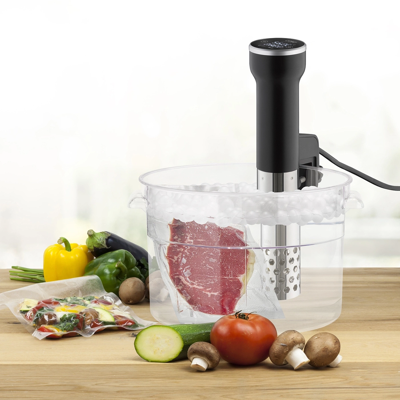 Sous-Vide-Gerät mit Fleisch und Gemüse auf einem Holztisch