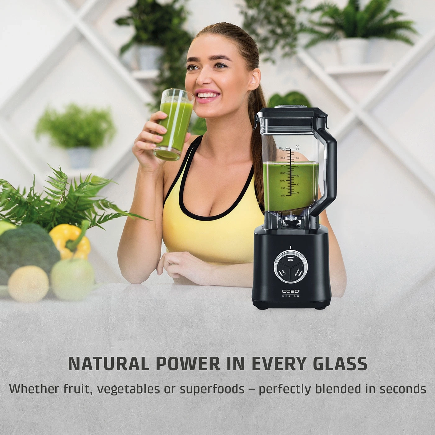 Young woman drinks green smoothie next to a blender and fresh fruit.