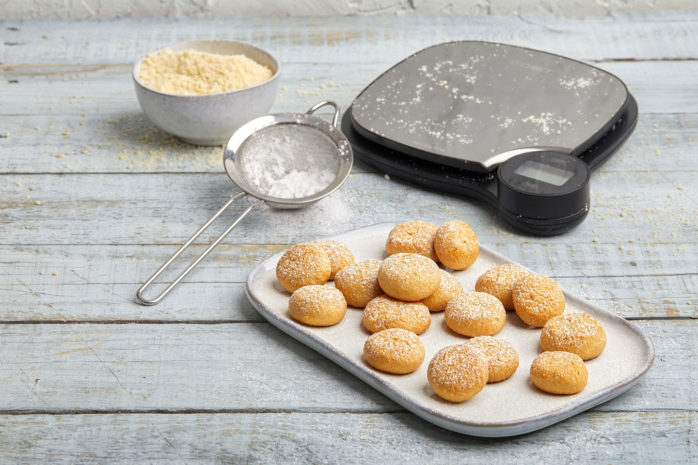 Cookies with powdered sugar on a plate, scale, flour, and sieve.